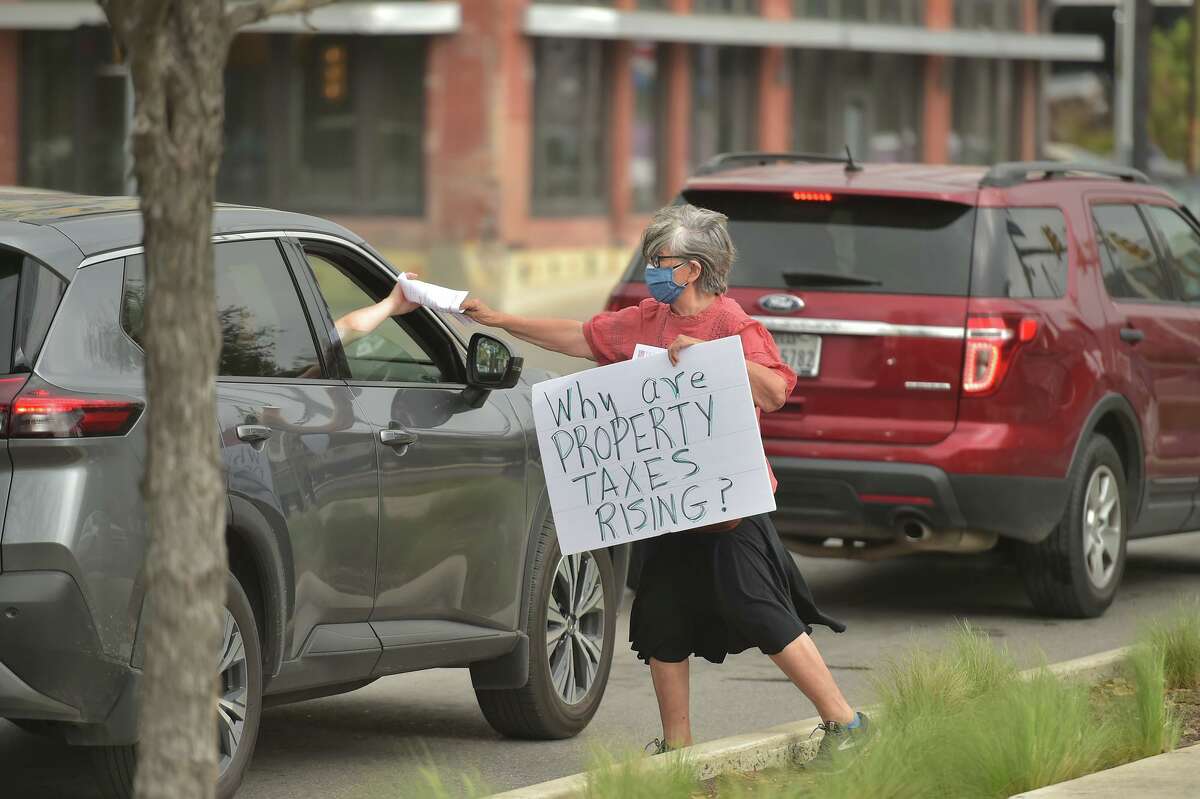 Rebecca Flores hands out literature to a motorist during a protest against rising property taxes and corporations getting tax breaks Saturday in San Antonio.