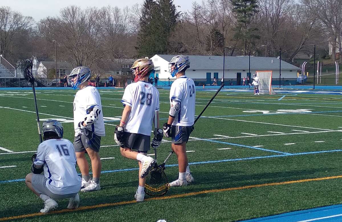 Goalie Aaron Garnett (28) and defender Adrian Rivera (24) talk on the sideline at Bunnell High School in Stratford, Conn., on April 14, 2022. They play for the co-op team between the town's two high schools, Bunnell and Stratford. Garnett's helmet is in Stratford colors; Rivera's is in Bunnell colors.