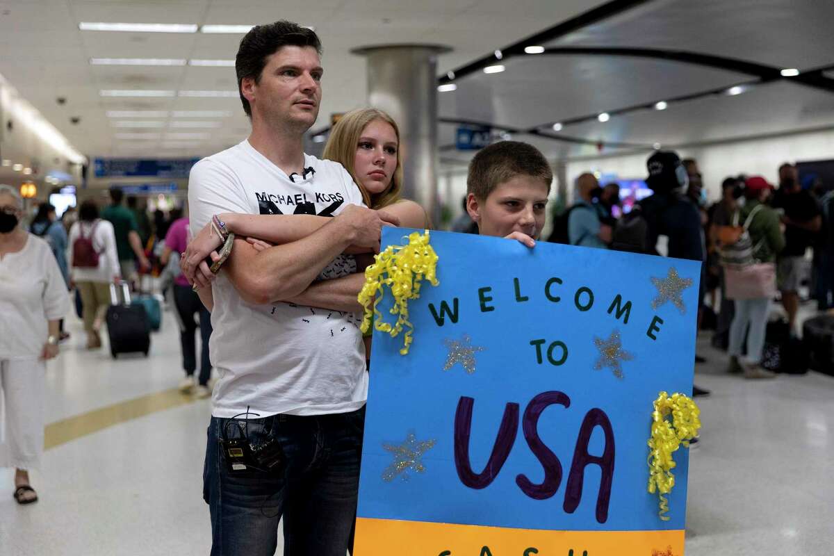 Ivana Kovalska, 15, hugs her dad, Dmytro Kovalskyy, while her younger brother, Radomyr Kovalskyi, 11, holds a sign they made welcoming their cousins arriving from Ukraine at San Antonio International Airport.