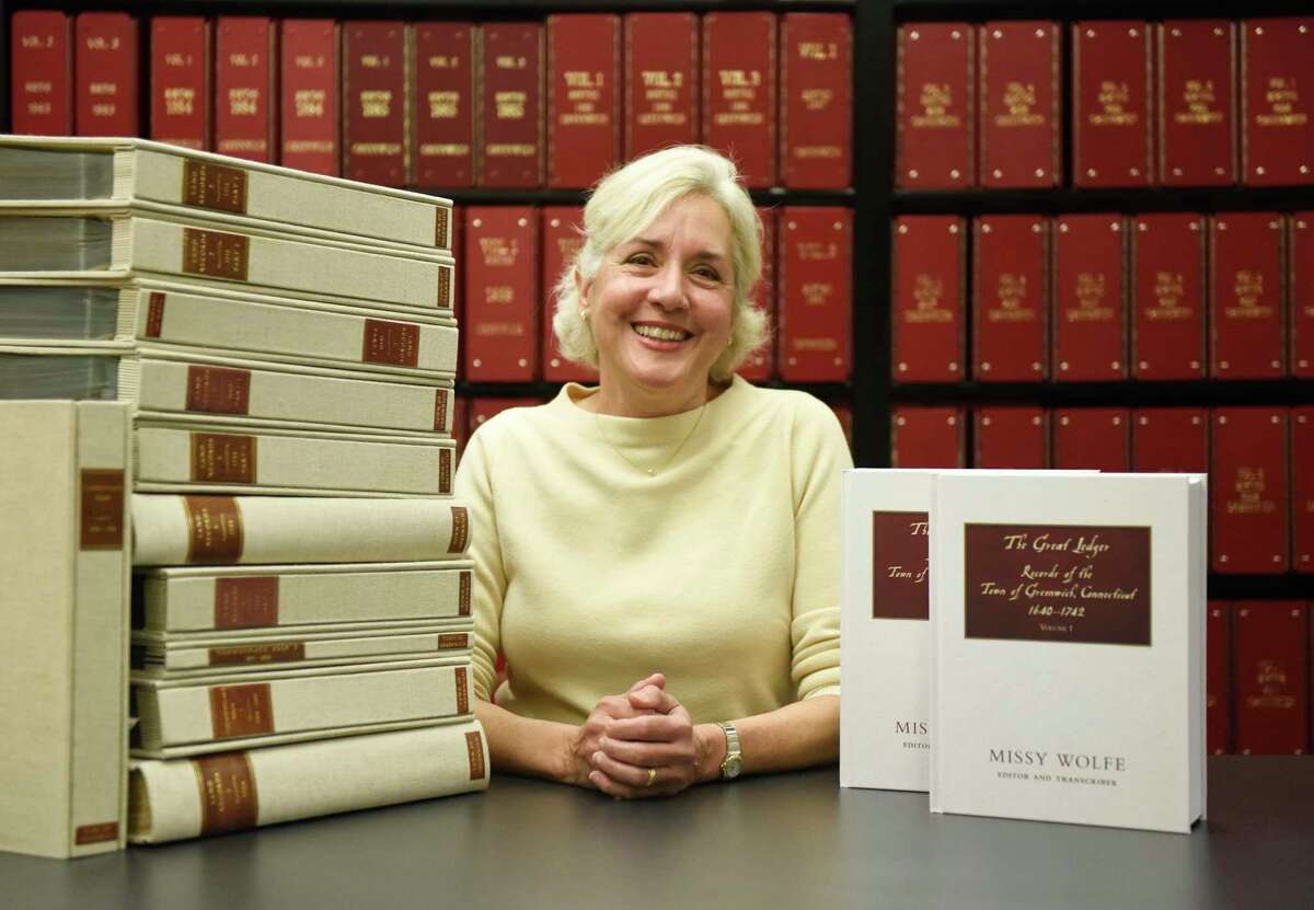 Historian Missy Wolfe poses beside Greenwich original historical documents, left, and her new book "The Great Ledger: Records of the Town of Greenwich Connecticut 1640-1742" in the town archives at Town Hall in Greenwich, Conn. Thursday, April 14, 2022. Wolfe has transcribed hundreds of pages of Greenwich's historical documents from the 1600s and 1700s into a concise and accurate historical record.