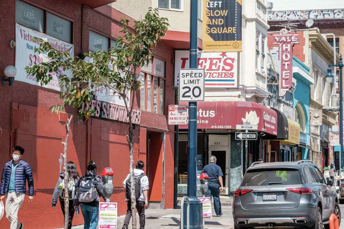 Pedestrians walk near a 20 mph speed limit sign in the Tenderloin neighborhood of San Francisco on August 26, 2021.
