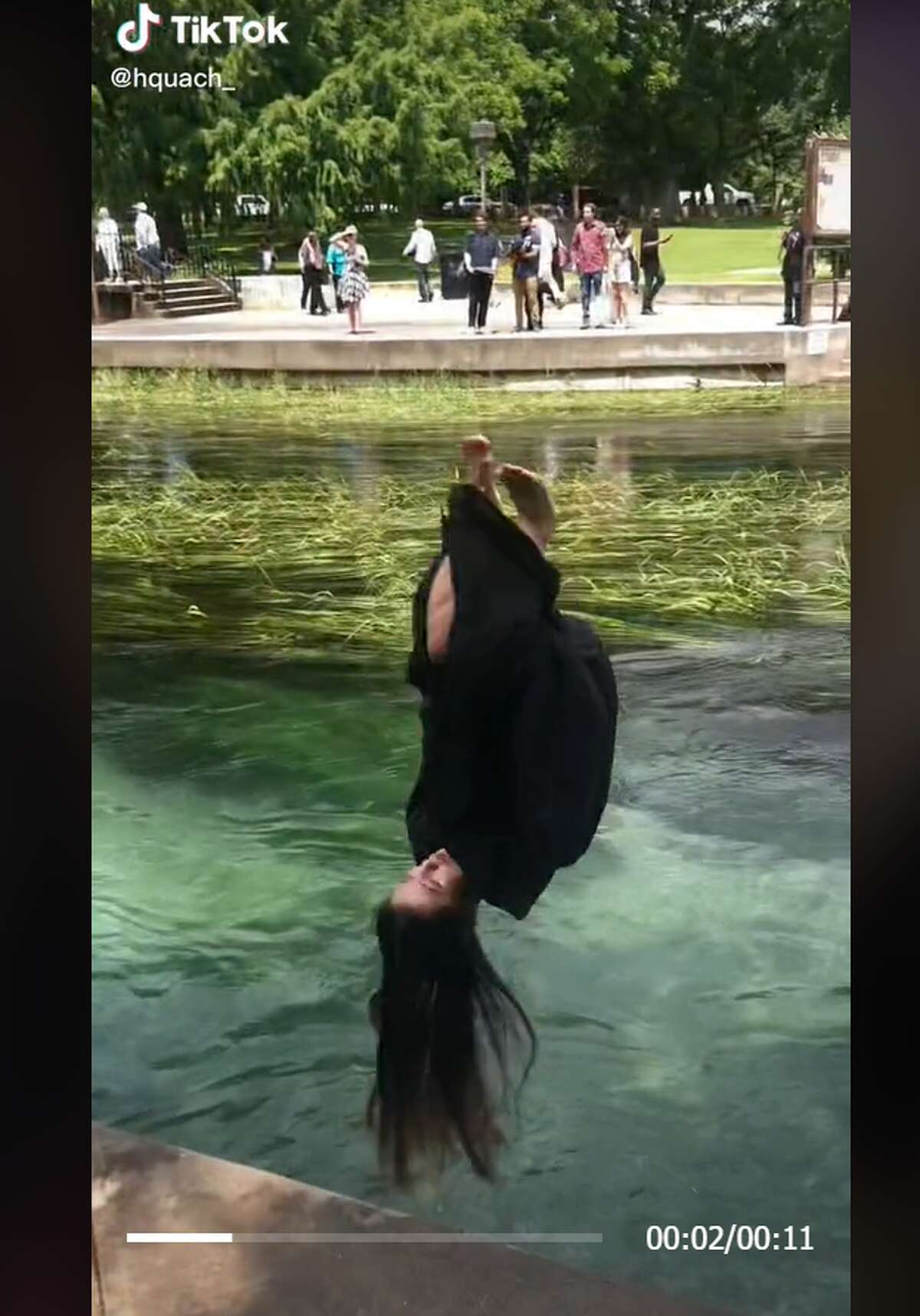 A screenshot of a TikTok video showing a Texas State University graduate from 2019 flipping into the river after commencement.