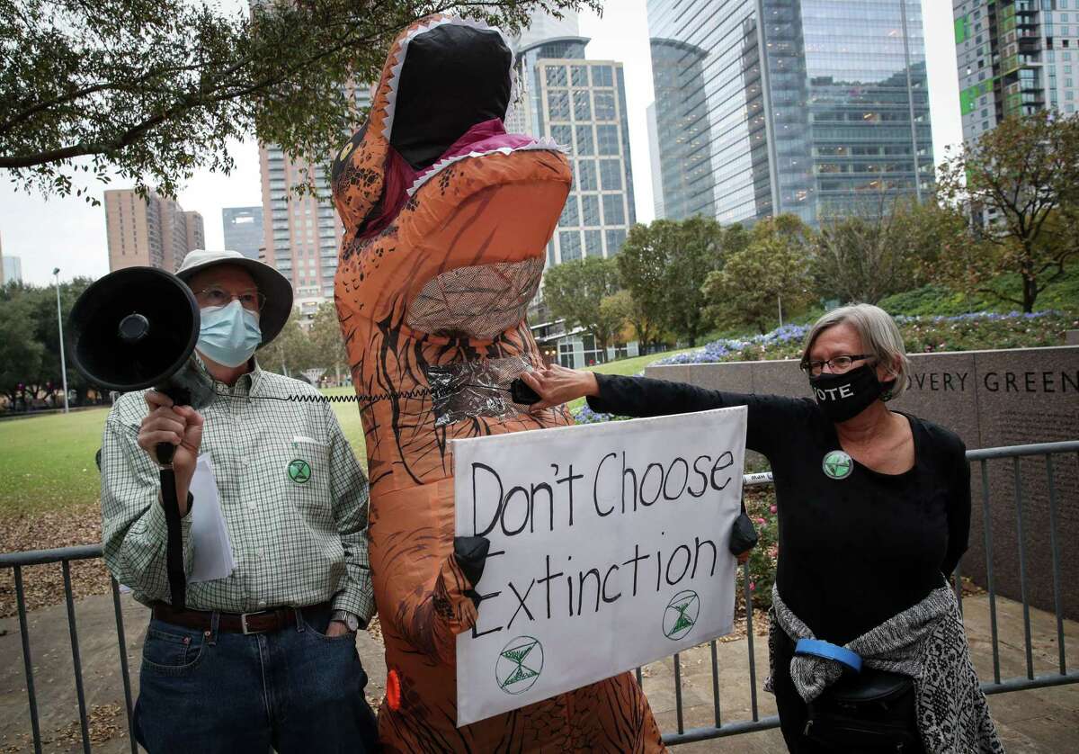 Bob Henschen, left, and Gina Biekman help a woman in a dinosaur costume use a megaphone to protest at the 23rd World Petroleum Congress on Tuesday, Dec. 7, 2021, at George R. Brown Convention Center Houston.