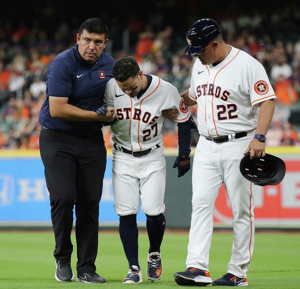 HOUSTON, TEXAS - APRIL 18: Jose Altuve #27 of the Houston Astros is helped off the field by first base coach Omar Lopez #22 and a trainer after injuring himself running out an infield hit in the eighth inning against the Los Angeles Angels at Minute Maid Park on April 18, 2022 in Houston, Texas.