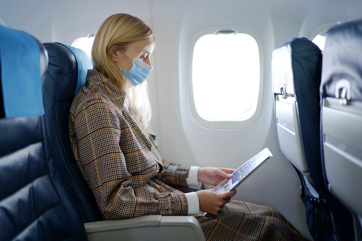 Portrait of woman wearing mask inside airplane while reading safety instructions.