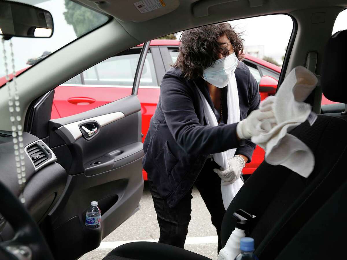 Rosa Mendoza, who drives for Uber and Lyft, cleans her car with disinfectant in San Francisco, in 2020. On Tuesday, the state cited Uber and Lyft for safety violations pertaining to how the companies treated their drivers.