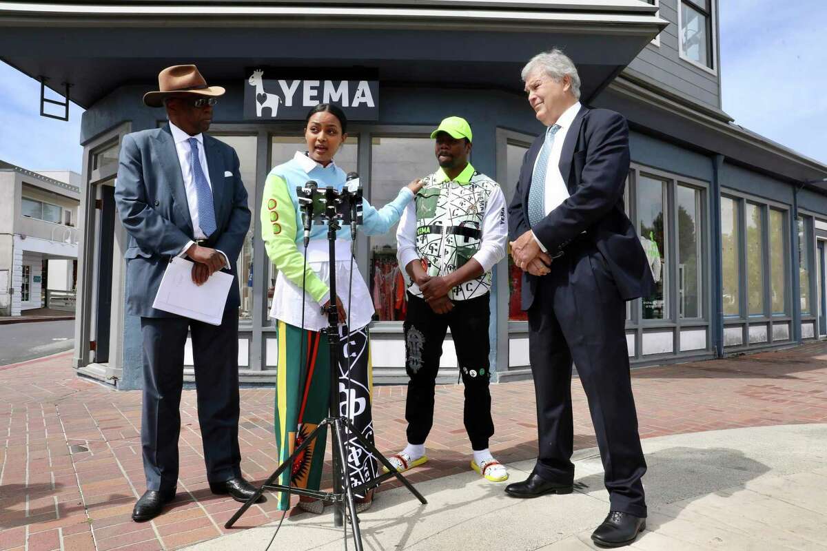 Hawi Awash, second from left, speaks during a press conference with her husband Yema Khalif, third from left, and their attorneys Charles Bonner, left, and David C. Anderson, right, Tuesday, April 19, 2022, in Tiburon, Calif. The couple were working at their boutique clothing store, YEMA, late one night in 2020 when officers asked them to prove it was theirs. Two years later, the couple and town officials gathered to announce a series of reforms resulting from that incident.