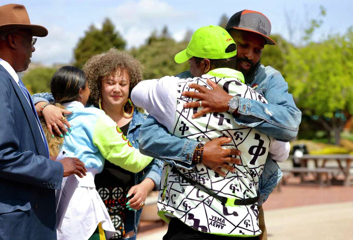 Paul Austin, right, hugs his friend Yema Khalif following a press conference outside of the boutique clothing store Khalif owns with his wife, Hawi Awash, on Tuesday, April 19, 2022, in Tiburon, Calif. After threatening a federal lawsuit over an August 2020 racial profiling incident, Khalif and Awash instead worked directly with town officials to enact policing reforms, including the formation of a citizens review board.