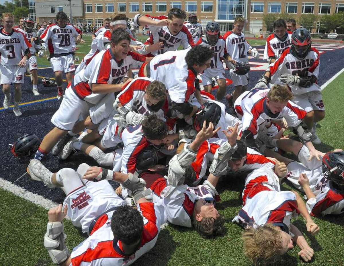 New Fairfield High School players run from the bench and pile on goalkeeper Brennan Hart (20) after winning the boys lacrosse Class M State Championship by defeating Daniel Hand 13 to 11. Saturday, June 9, 2018, at Brien McMahon High School, Norwalk, Conn