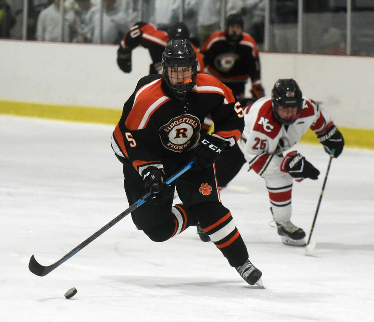 Ridgefield senior Henry Garlick (5) brings the puck through the neutral zone, as New Canaan’s Carter Spain (25) pursues during Tuesday’s boys ice hockey game at the Darien Ice House.