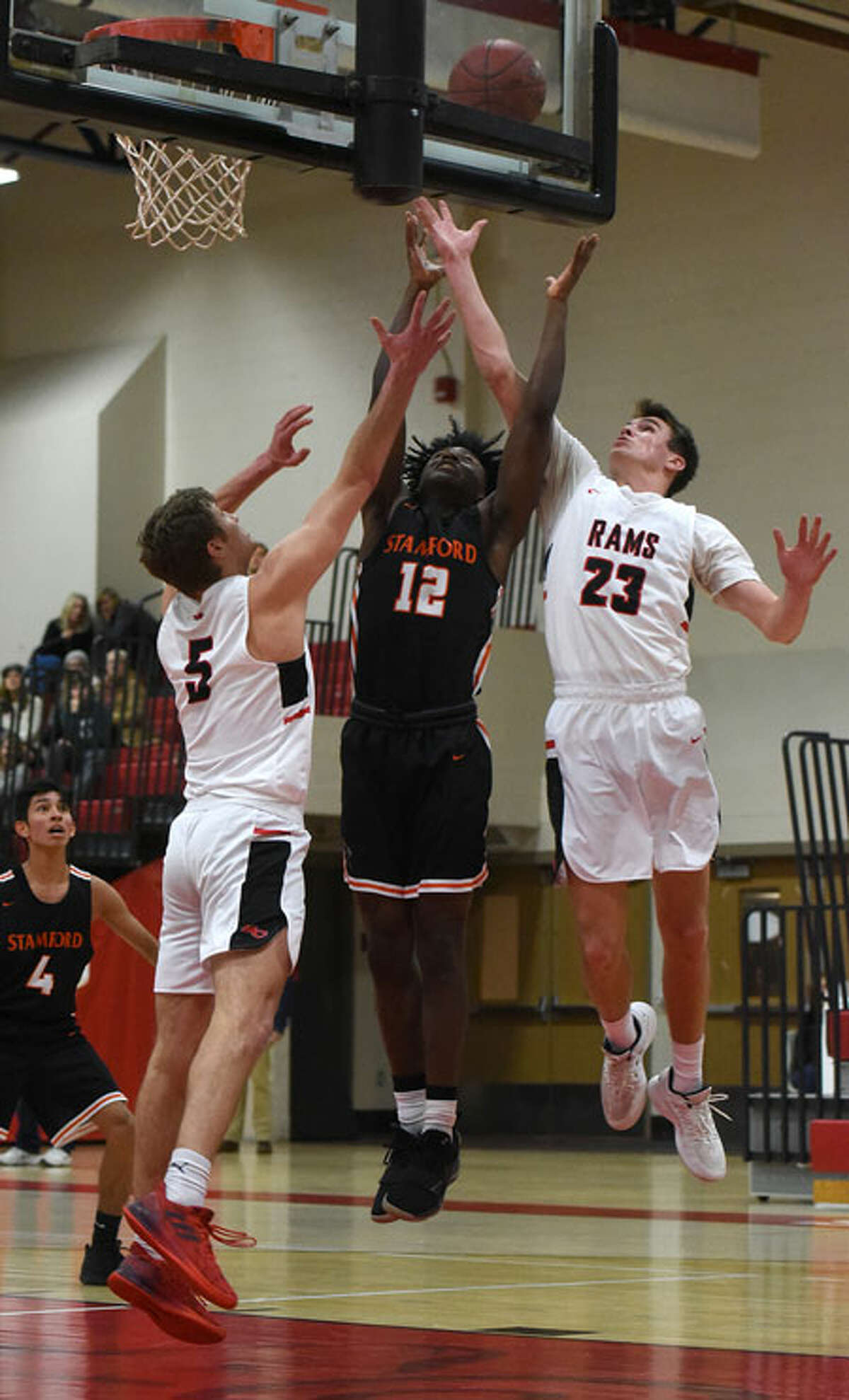 New Canaan’s Jack Richardson (23) and Alex Gibbens (5), along with Stamford’s Danny Simms (12), go up for a rebound on Thursday, Jan. 10, at NCHS.