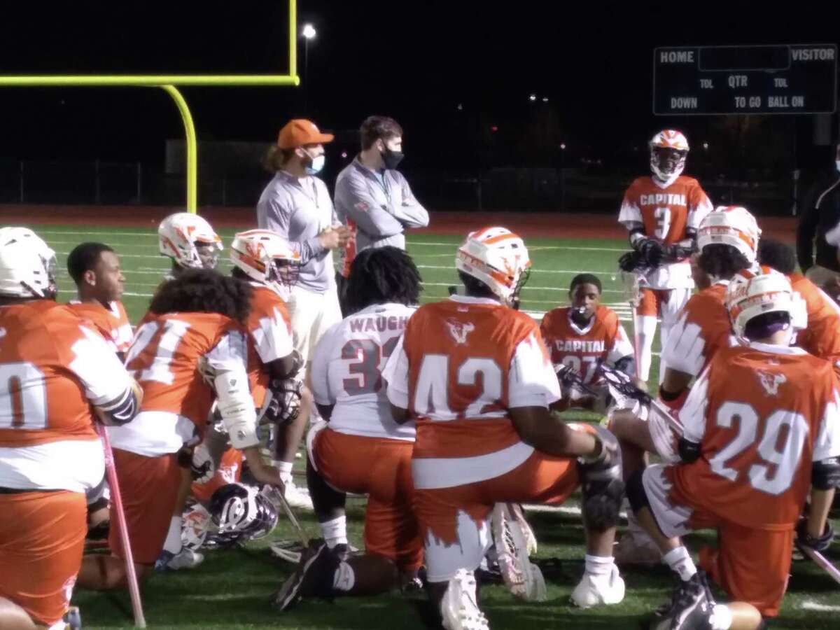 The Capital Prep/Classical boys lacrosse team huddles around coach Lee Mascolo (orange cap) after an 11-3 win over Wilbur Cross at Bowen Stadium in New Haven, Conn., on April 20, 2021.