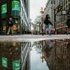 Pedestrians are reflected in a puddle as they cross the street in downtown San Francisco on Monday, March 28, 2022. More rain was likely in store for the Bay Area. Further north, in the Sierra, meteorologists expected a deluge of snow expected to significantly impact travel conditions.