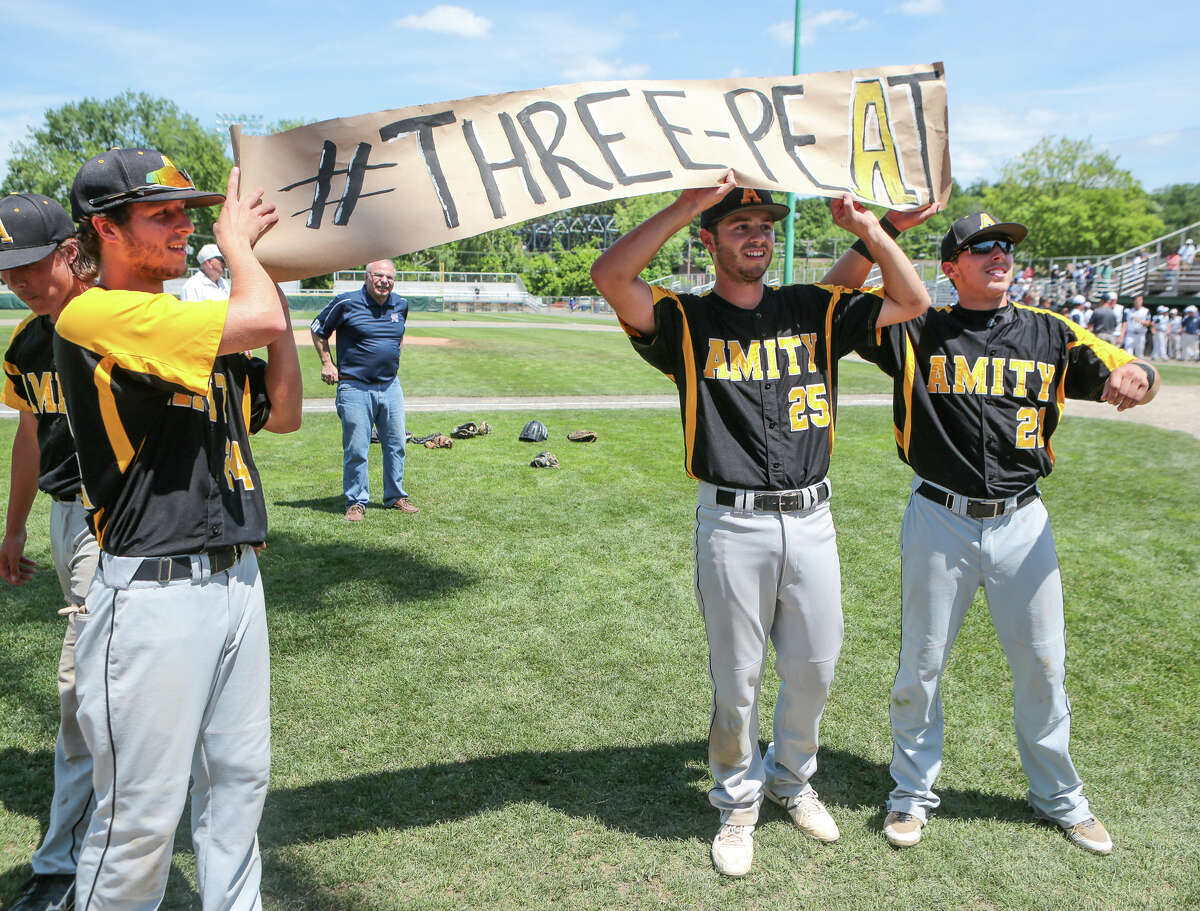 Kyle Mattei (left), Amity’s baseball players hold up a ‘THREE-PEAT’ sign following their third-consecutive Class LL baseball championship, 8-1 over Staples (Photo John Vanacore)