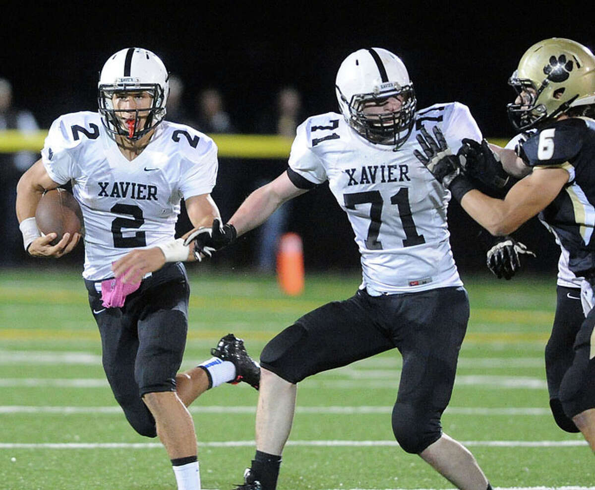 Photo by Peter Casolino-Register/ Xavier quarterback Joe Carbone looks for room as he gets a block from Riley Byrne during the first quarter of Friday night’s win over Hand.