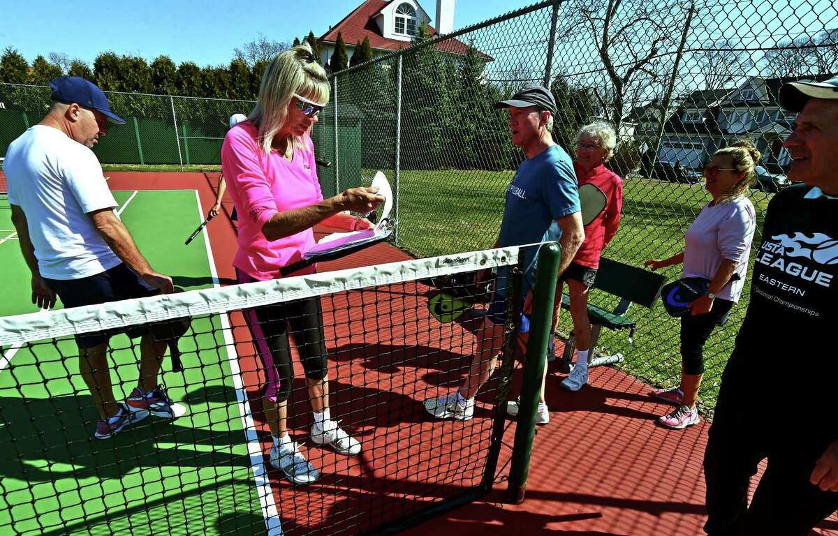 Leader Betsy Underhill , with clipboard, assigns teams during games of pickleball on the tennis courts at Loughlin Avenue Park in Greenwich, Conn., on Friday March 18, 2022. Pickleball, a sport gaining in popularity in the town, has plenty of seniors seeking to support and protect proposed funding for it in the upcoming town budget.