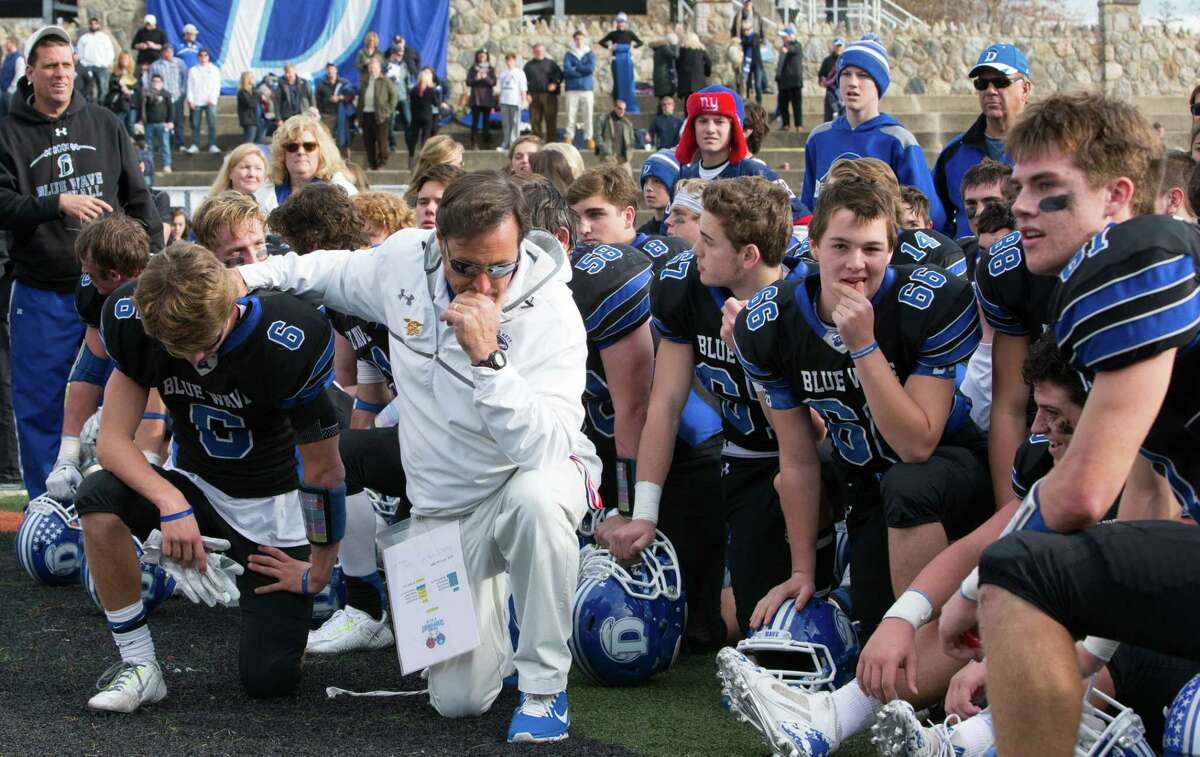 Darien coach Rob Trifone (in white) kneels with 2015 captain Colin Minicus (6) and the rest of the Blue Wave football team following last year’s FCIAC Championship / Turkey Bowl victory over New Canaan (Photo via Darien Athletic Foundation)