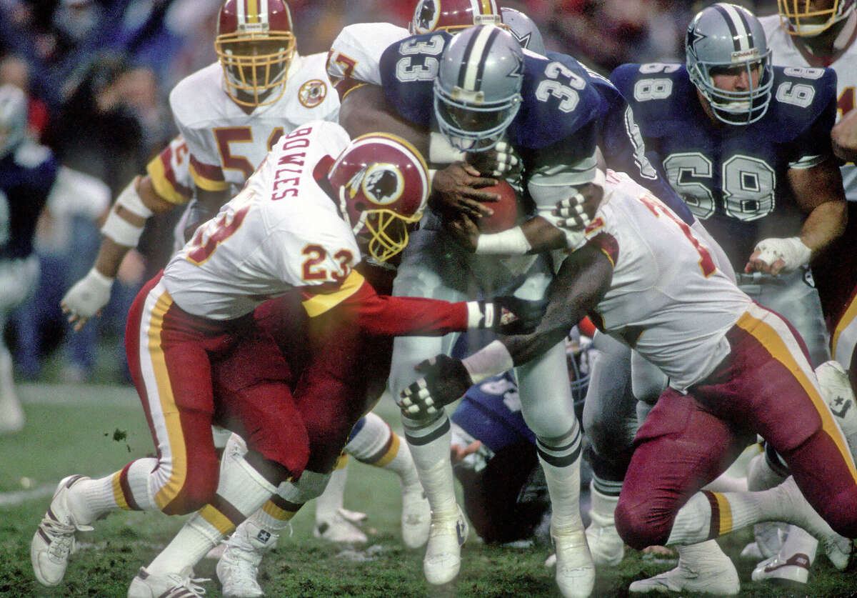 Running back Tony Dorsett #33 of the Dallas Cowboys is tackled by safety Todd Bowles #23 and defensive linemen Darryl Grant #77 and Dexter Manley #72 of the Washington Redskins during a game at RFK Stadium on November 23, 1986 in Washington, DC. The Redskins defeated the Cowboys 41-14.