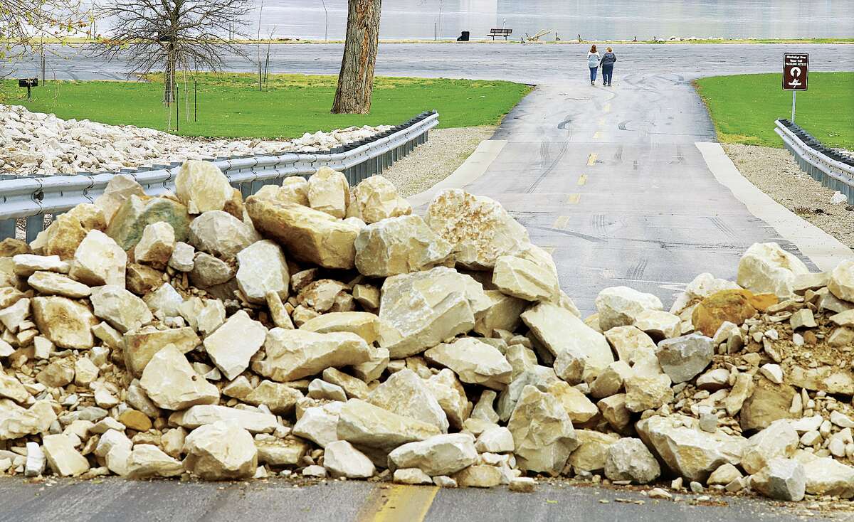 Two people walk down the entrance road to the Lincoln Shields Recreation Area Thursday past a locked gate and a large pile of rocks piled on the entrance road in West Alton, Missouri. A sign, posted by the Corps of Engineers River Project Office, says the popular river viewing area and boat launches are "locked until further notice."
