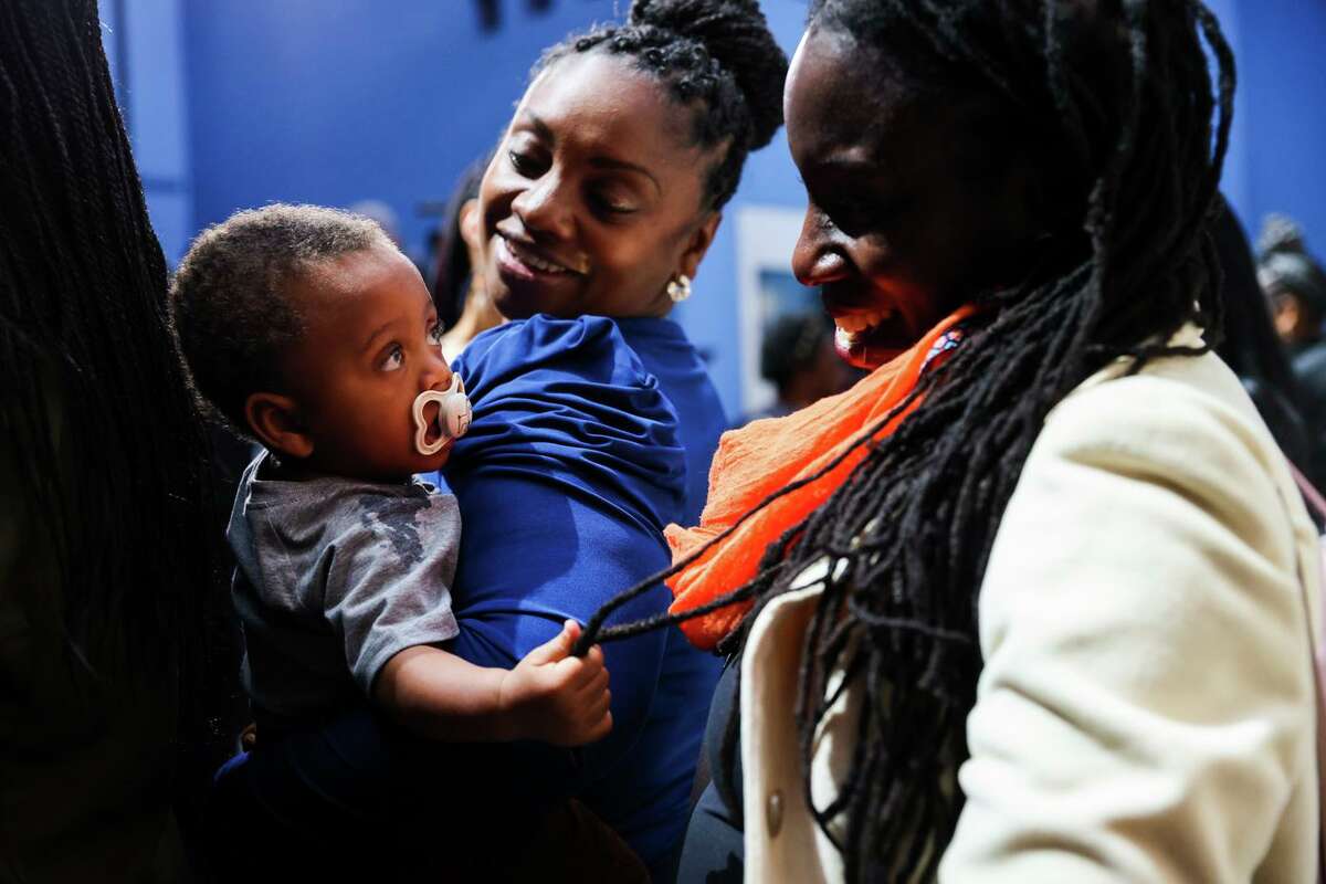 EMBRACE program member Hope Williams holds son Kingston Burt, 11 months, as he touches the hair of Ifeoma Udoh, a health equity researcher at ETR, after the vice president’s speech.