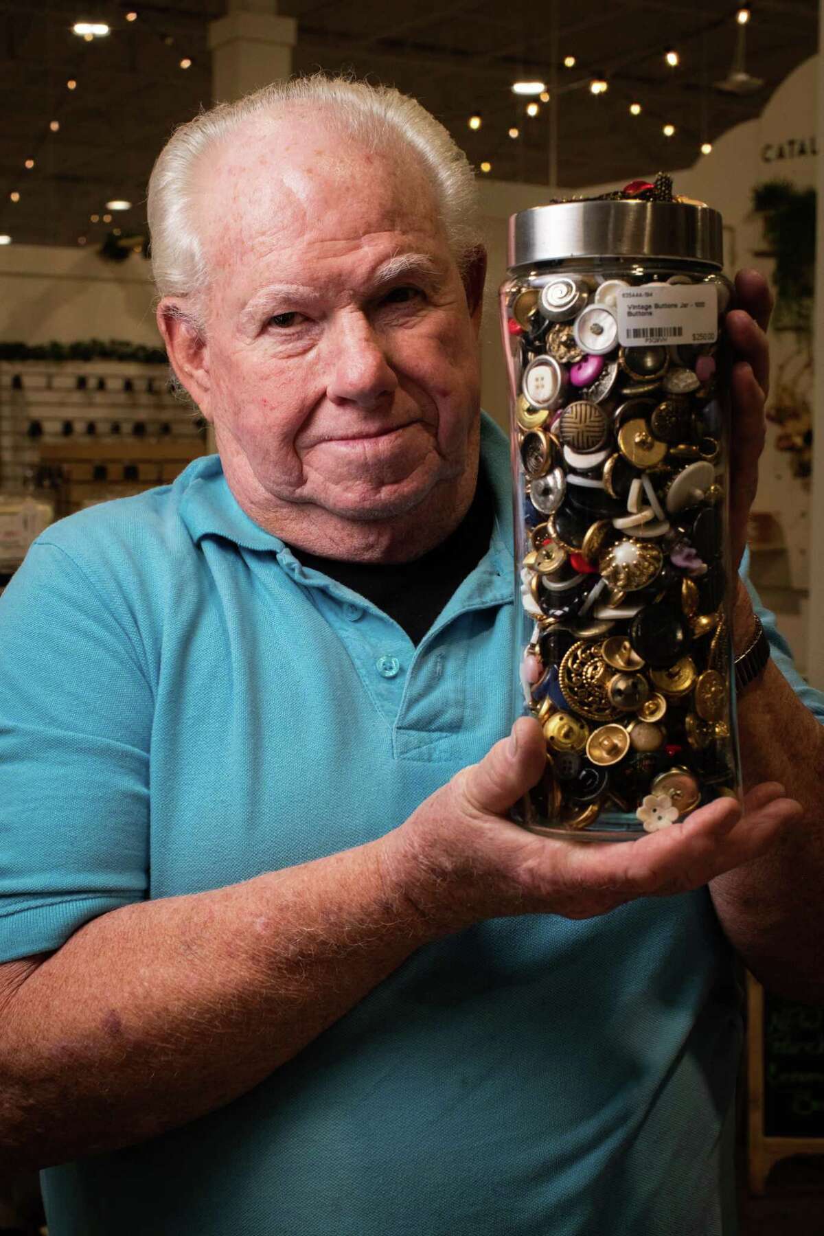 Dan Gorelick, 80, holds a container filled with buttons at his kiosk inside Cinco Ranch’s Painted Tree Boutiques.