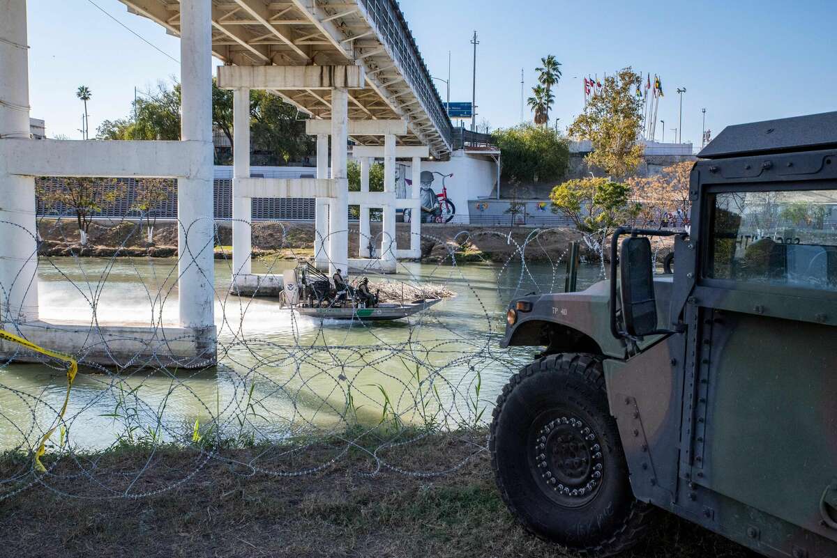 A Customs and Border Patrol boat travels past razor wire and a military vehicle down the Rio Grande river on November 19, 2021 in Eagle Pass, Texas.
