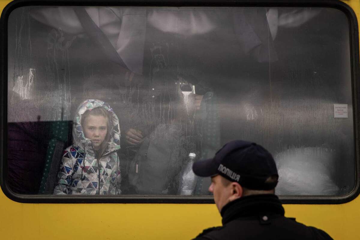 A police officer looks on as a girl from Mariupol looks out the window of a bus after a convoy of vehicles arrived at an evacuation point, carrying people from Mariupol, Melitopol and surrounding towns under Russian control on April 21, 2022, in Zaporizhzhia, Ukraine.