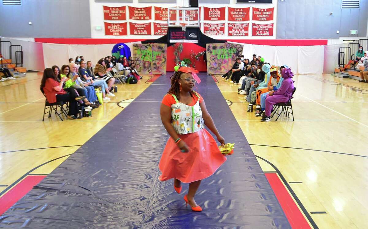 As part of J.M. Wright Technical High School's Earth Day Celebration, teacher Latrina Annosier models a bridesmaid dress made up of recycled materials during its "trashy" fashion show in the gymnasium in Stamford, Conn., on Friday April 22, 2022. Students have been tasked with creating wearable fashion using any type of recycled material, including plastic bags and bottles, packing materials, fabric scraps and swatches, coffee filters and cardboard.