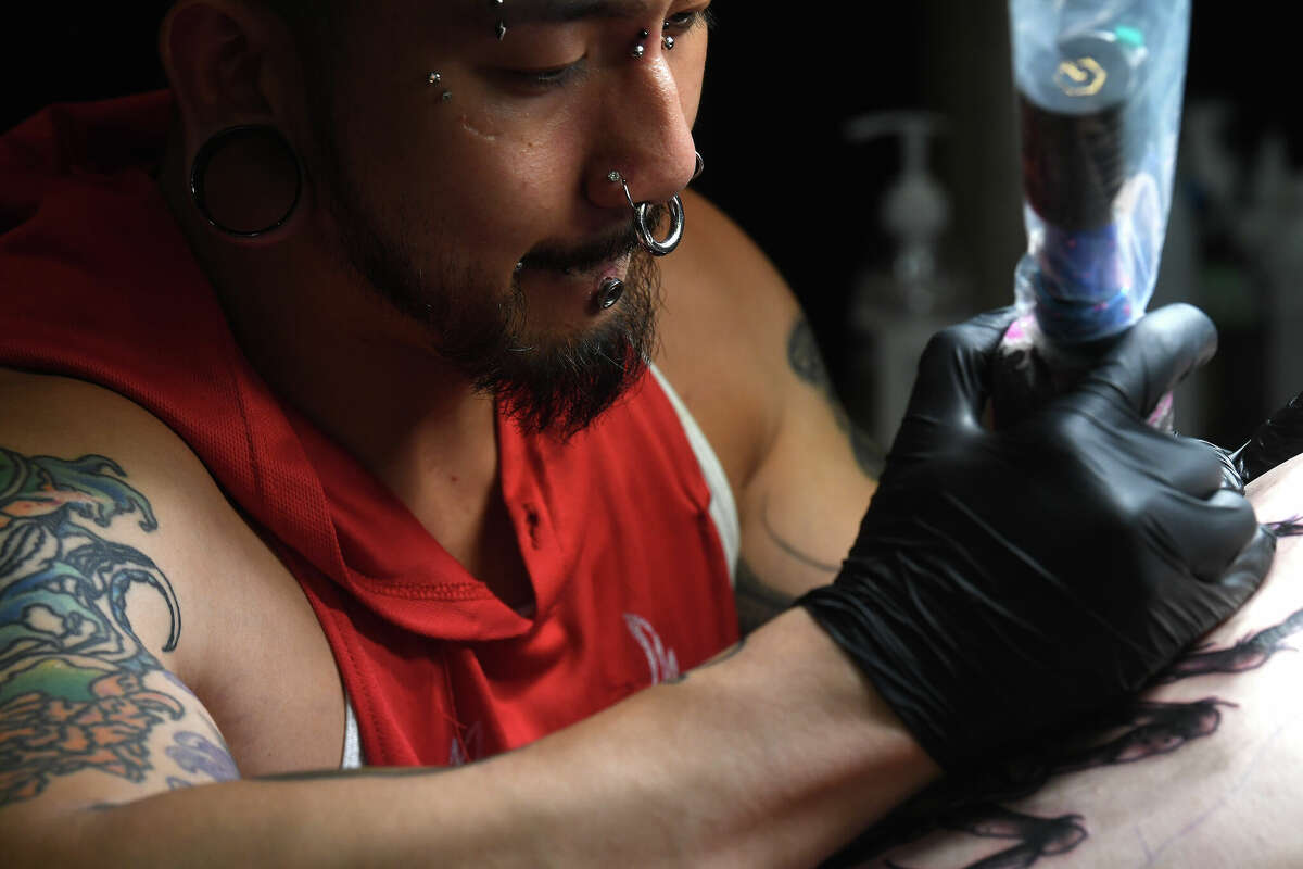 Beaumont artist Austin Pham does a leg piece for Audrey Anderson on the opening day of this Ink Masters Tattoo Convention that runs through Sunday at the MCM Elegante Hotel. Photo made Friday April 22, 2022. Kim Brent/The Enterprise