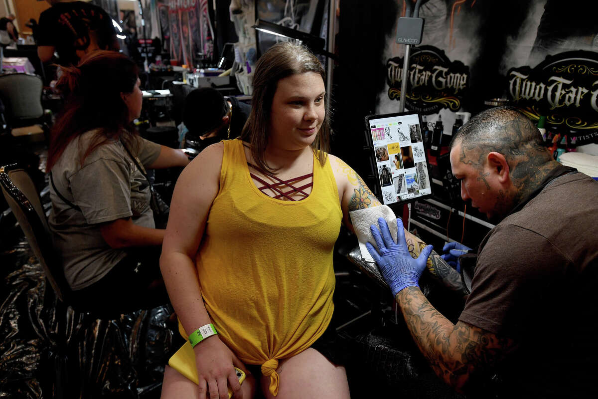 Kylie Andreu watches as "El Famous Cat" works on a floral piece on the opening day of this Ink Masters Tattoo Convention that runs through Sunday at the MCM Elegante Hotel. Photo made Friday April 22, 2022. Kim Brent/The Enterprise