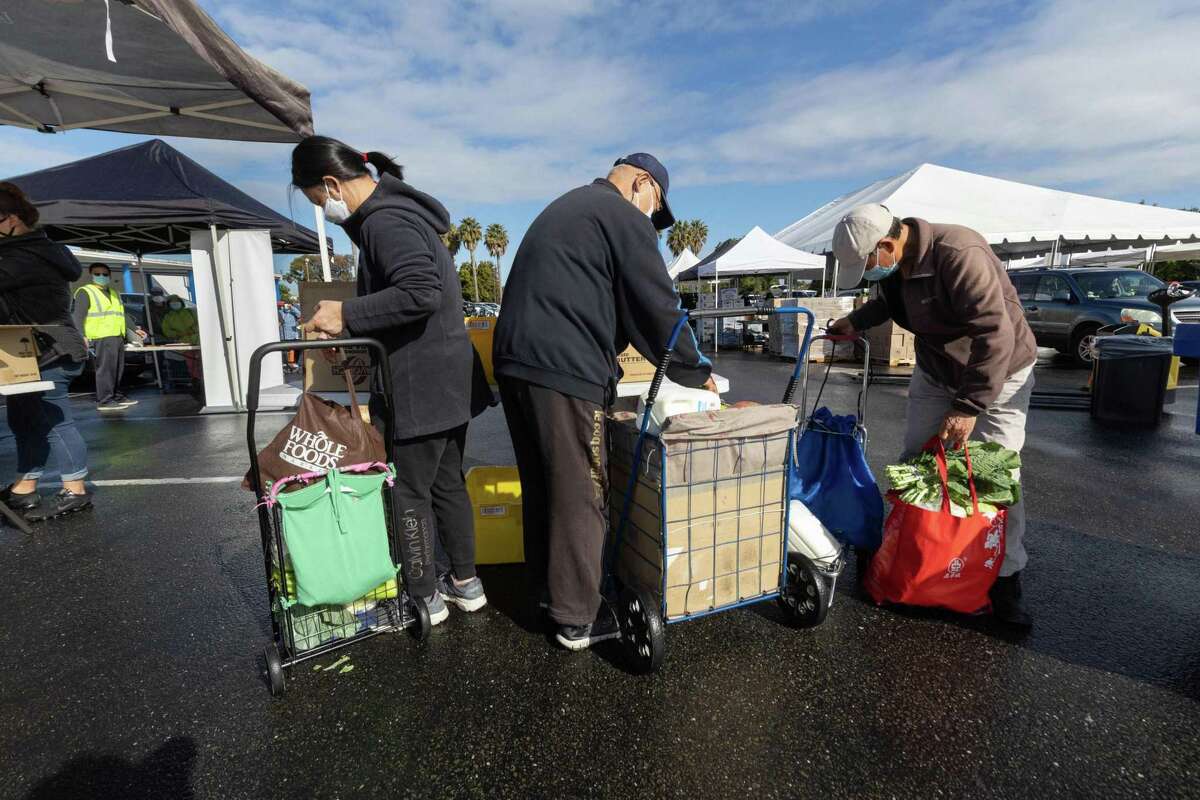 Sue Siu, left, steadies her cart at a food bank distribution site in Oakland on Friday, April 22, 2022.