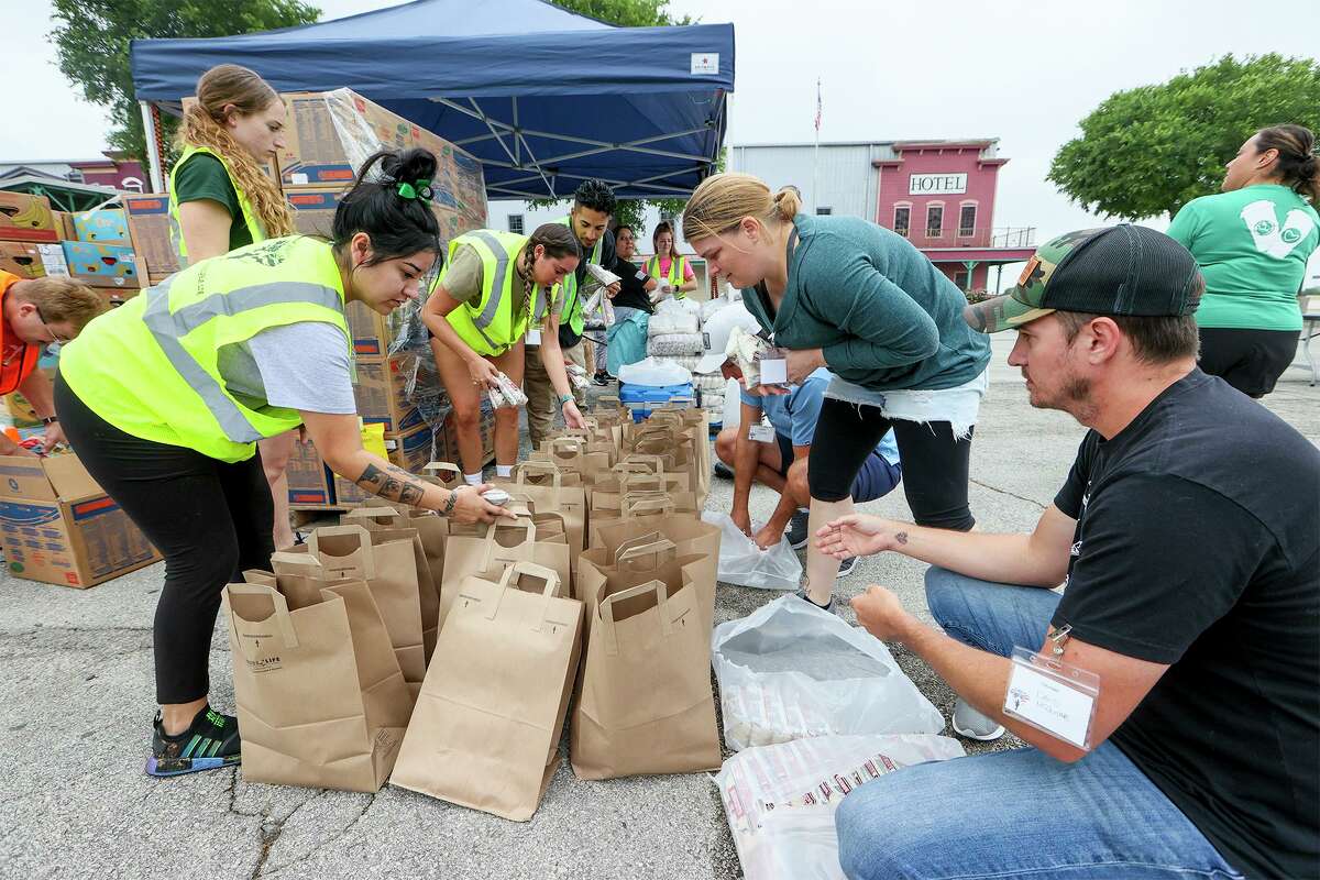 Volunteers put packages of rice in donation bags at a food station on April 21 during the monthly Soldiers’ Angels food pantry for veterans at Cowboys Dance Hall.