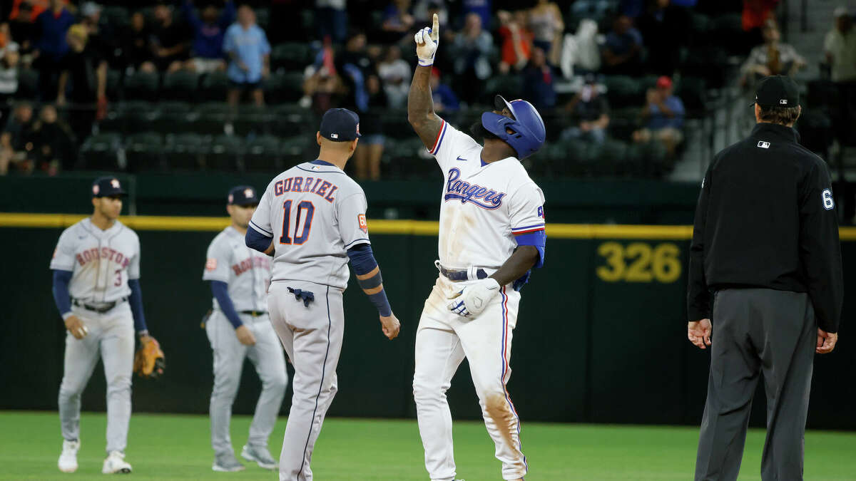 Texas Rangers' Adolis Garcia, center right, celebrates his double that resulted in three RBIs as Houston Astros first baseman Yuli Gurriel (10) awaits a throw during the eighth inning of a baseball game Monday, April 25, 2022, in Arlington, Texas. (AP Photo/Michael Ainsworth)