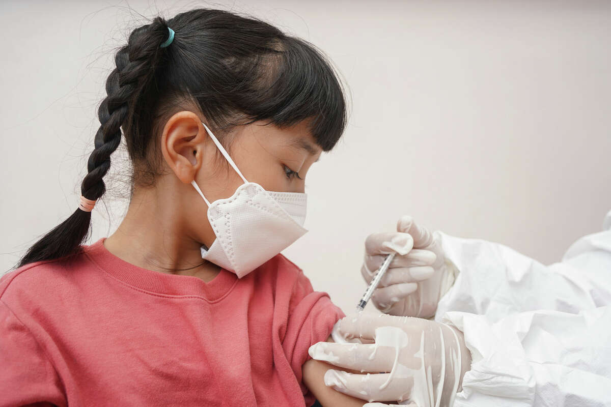 Little patient in face mask receiving coronavirus vaccine shot.