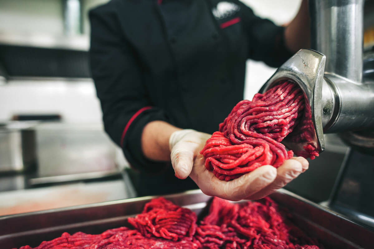 Male chef butcher doing fresh ground beef for burgers in the restaurant. He put small pieces of fresh beef meat in the grinder to make ground beef