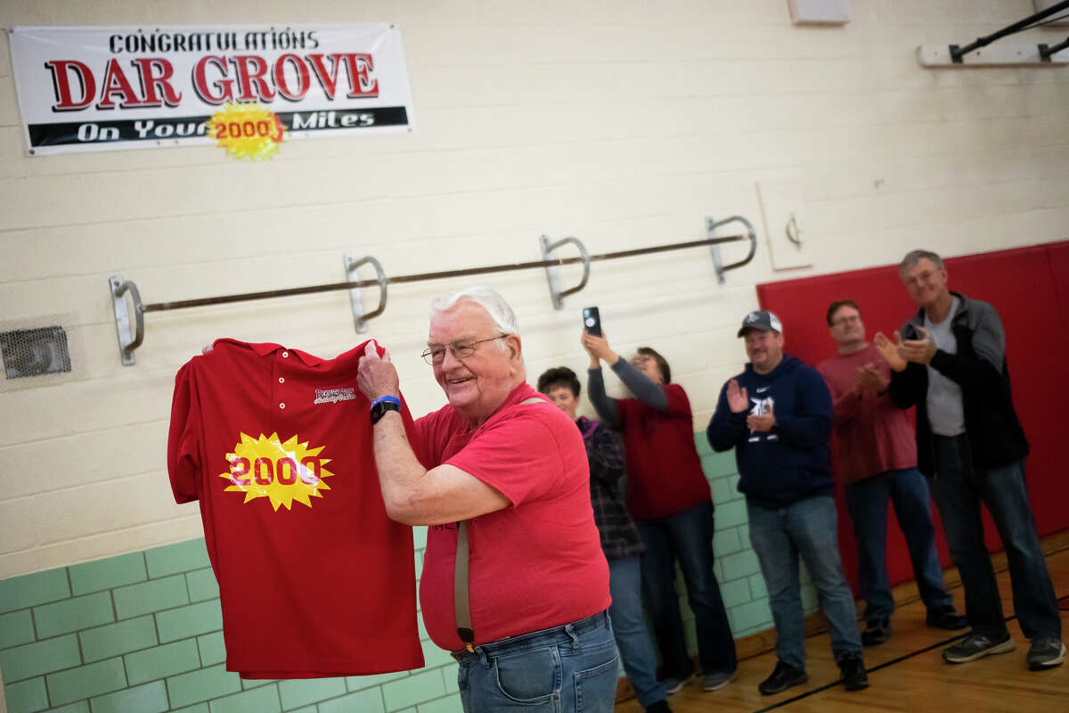 Dar Grove is gifted a celebratory shirt as he marks his 89th birthday Tuesday, April 26, 2022 by completing his 2,000th mile at the Beaverton Activity Center, with an entourage of fans walking with him.
