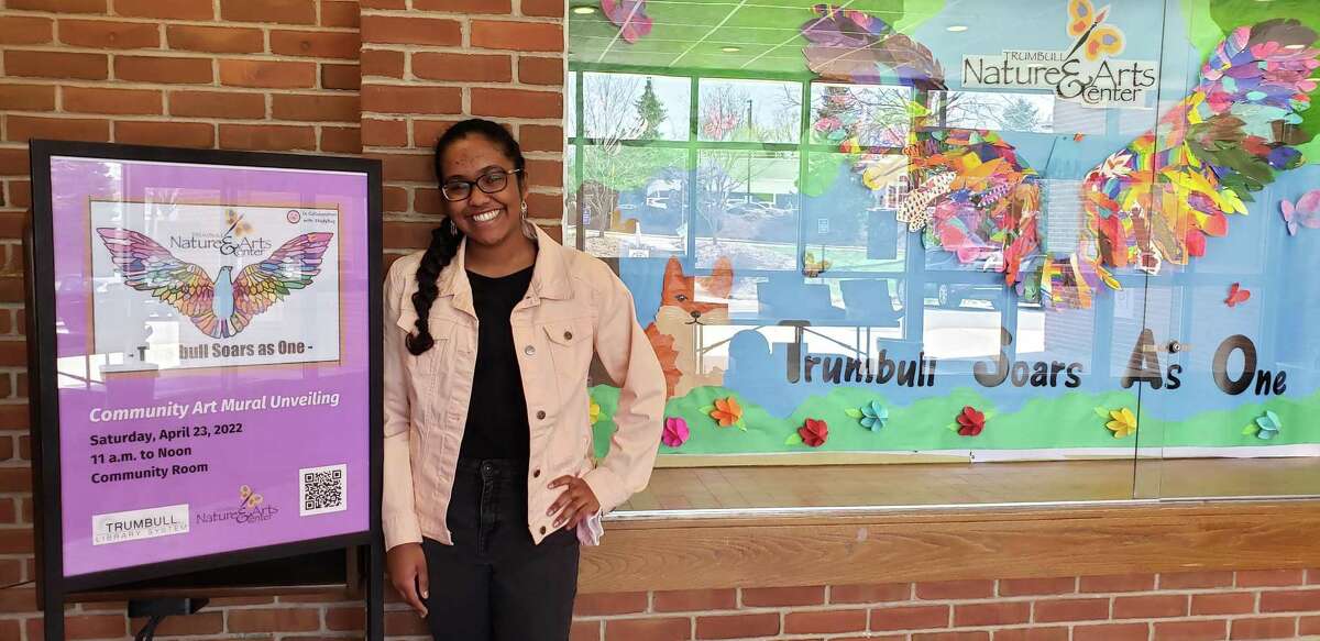 St. Joseph High School student Danielle Haniph, 17, stands with one of her “Trumbull Soars As One” murals at the Trumbull public library.