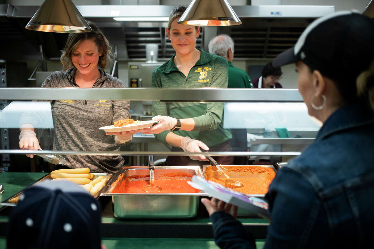 Dow High cross country coach Ashley Burr, center, and track and field coach Jamie Haruska, left, serve spaghetti and breadsticks to guests during Pasta with a Purpose, a fundraising event for the Dow High Sports Booster Club Tuesday, April 26, 2022 at the school in Midland.