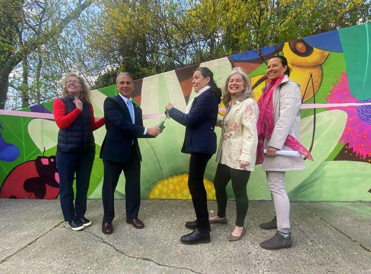 From left, Selectwoman Lauren Rabin, First Selectman Fred Camillo, mural and pollinator garden leader Myra Klockenbrink, Selectwoman Janet Stone-McGuigan, and environmental analyst Aleksandra Moch cut the ribbon at the unveiling of the pollinator pathway garden and mural at the bus stop across from Cardinal Stadium on East Putnam Avenue in Greenwich, Conn. Wednesday, April 27, 2022. The colorful mural depicting a garden scene was recently completed by Nelson "Cekis" Rivas and his assistant Yedi. Beside the mural and bus stop, invasive species were cleared to make room for native shrubs, herbaceous plants, bulbs and vines.