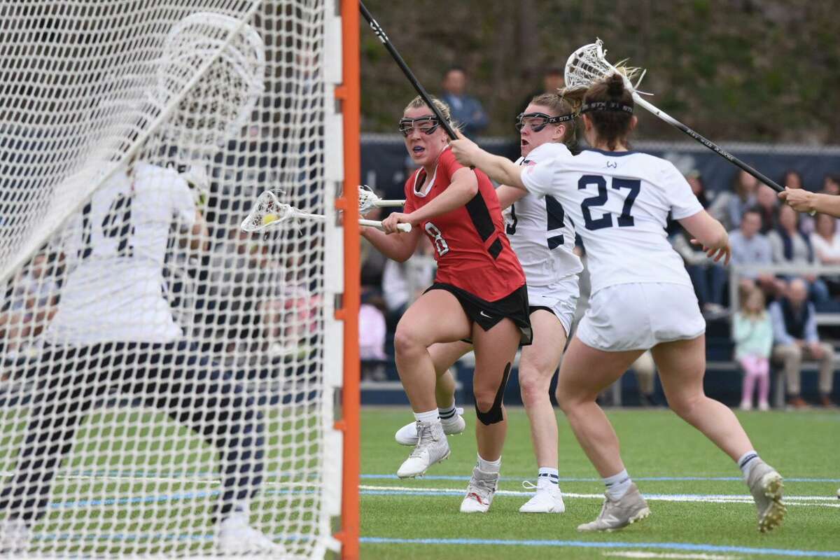 New Canaan’s Devon Russell (8) takes a shot against Wilton goalie Amelia Hughes while defended by Catherine Dineen (3) and Whitney Hess (27) during a girls lacrosse game on Wednesday, April 13, 2022 in Wilton, Conn.