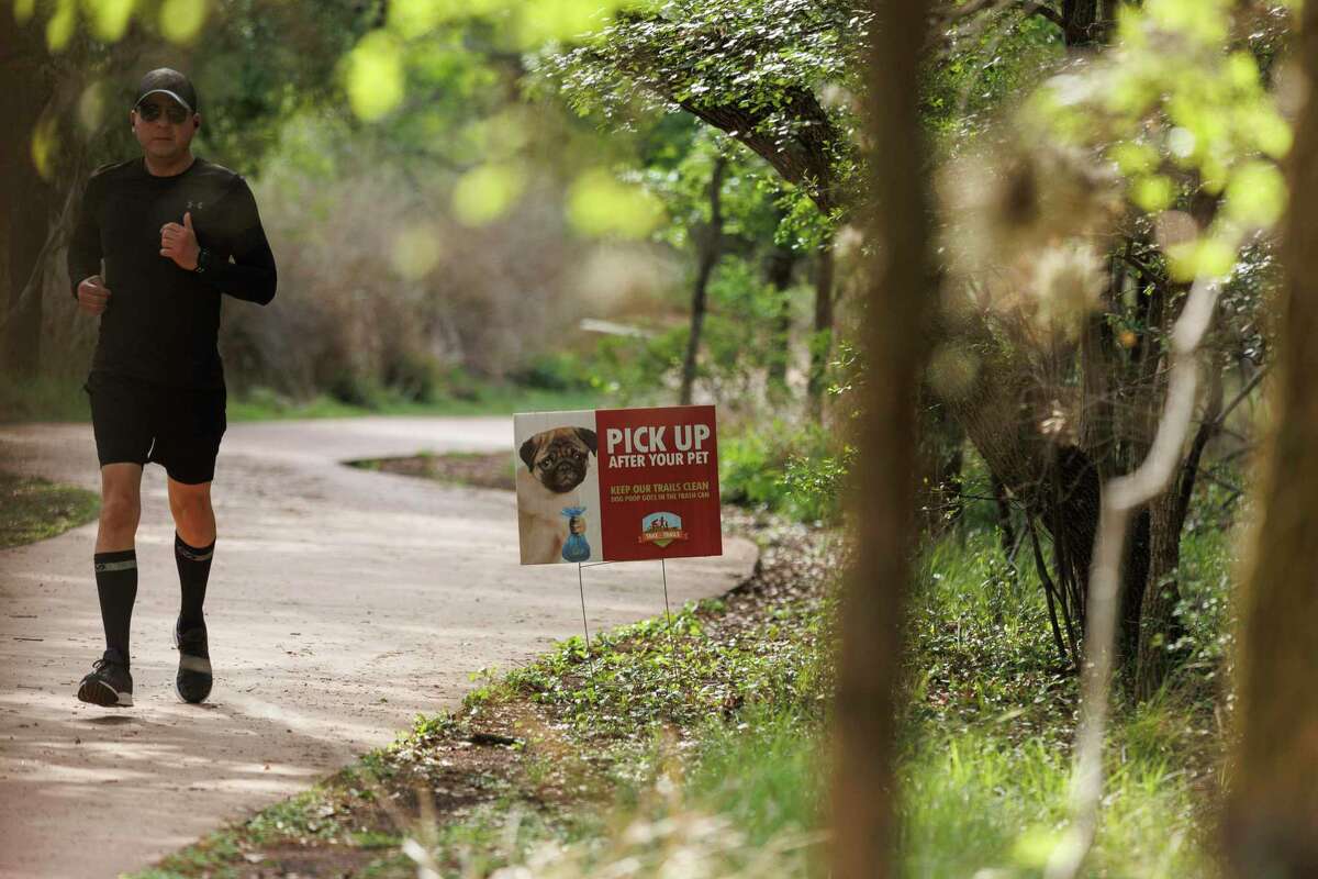 A runner passes a sign reminding dog owners to pick up dog poop along the Water Loop Trail in Phil Hardberger Park on Wednesday morning.
