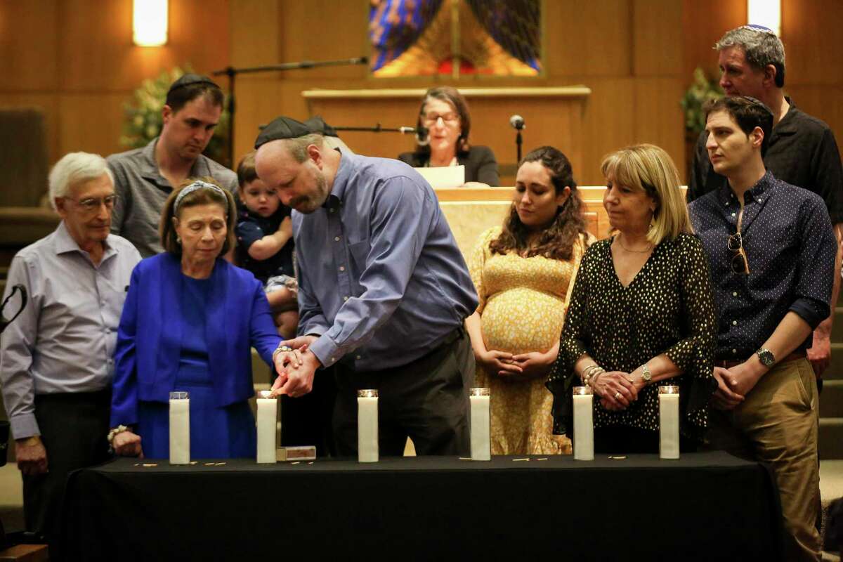 David Streusand, center-left, and his sister Charlotte Goldberg light a candle for their mother, a Holocaust survivor who lost many of her loved ones, during a Yom HaShoah ceremony for Holocaust Remembrance Day on Sunday, April 24, 2022, at Congregation Beth Israel in Houston.