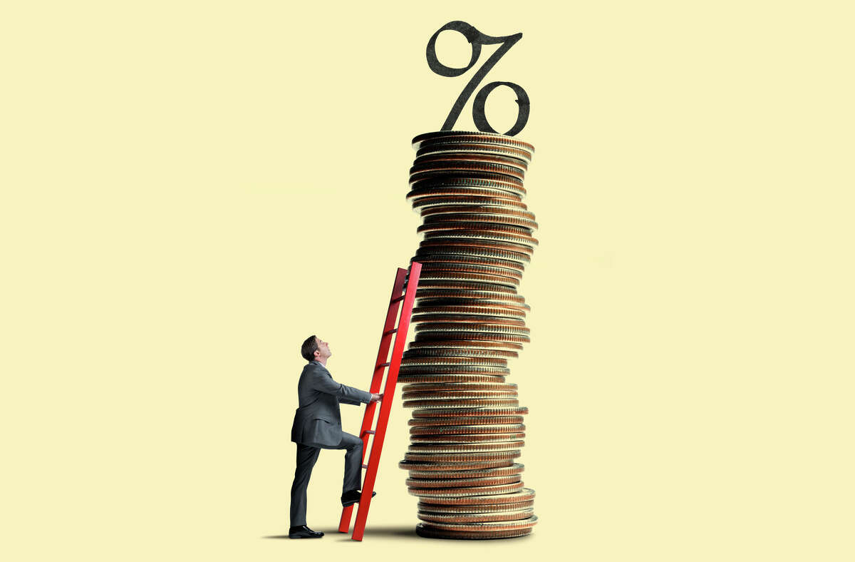 A man looks up as he leans a red ladder against a tall stack of coins that is topped with an interest rate symbol. Getty 