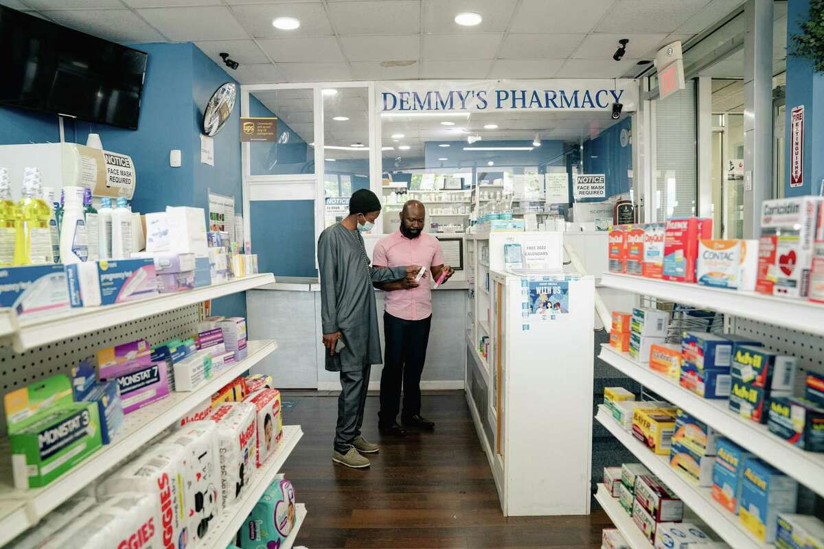 Dr. Adeolu Odewale, right, who has the new antiviral medication Paxlovid, helps a customer at his pharmacy in Greenbelt, Md., April 22, 2022. A national rollout of the first-of-its-king treatment has been far more complicated and less efficient than expected, leaving hundreds of thousands of courses unused as cases of the Omicron subvariant BA.2 surge. (Shuran Huang/The New York Times)