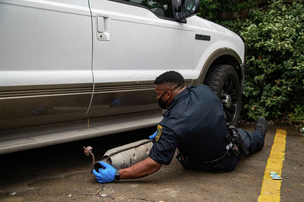A Houston police officer pulls out a stolen catalytic converter after checking under a vehicle as part of an investigation, Friday, June 4, 2021, in Houston.