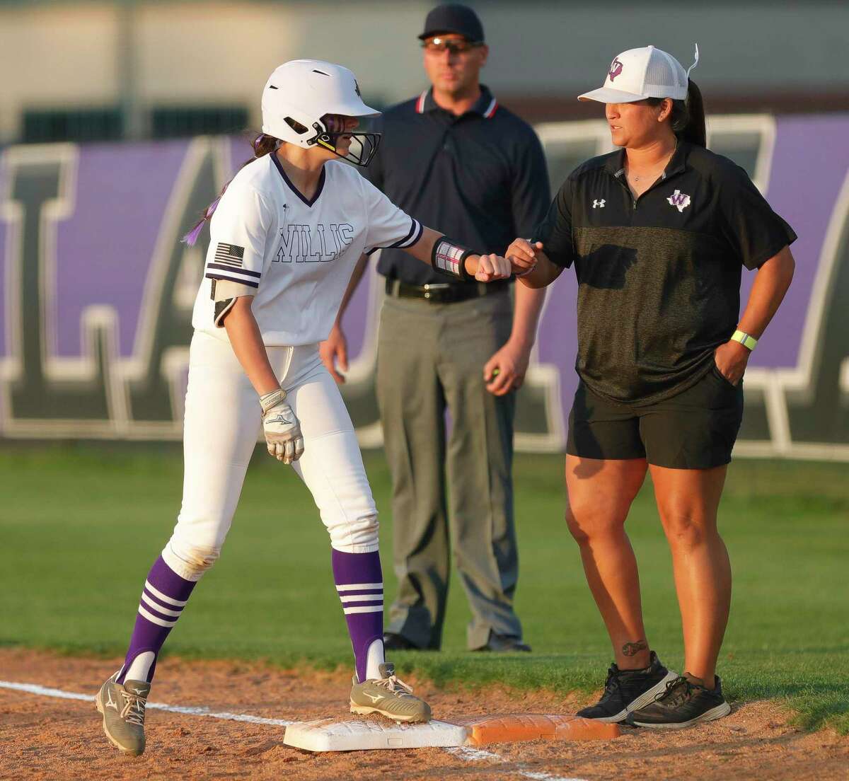 Mazlyn Heyer #24 of Willis gets a fist-bump from first base coach Lee Lara after hitting a single in the second inning of a Region III-6A high school softball bi-district playoff game at Willis High School, Thursday, April 28, 2022, in Willis.