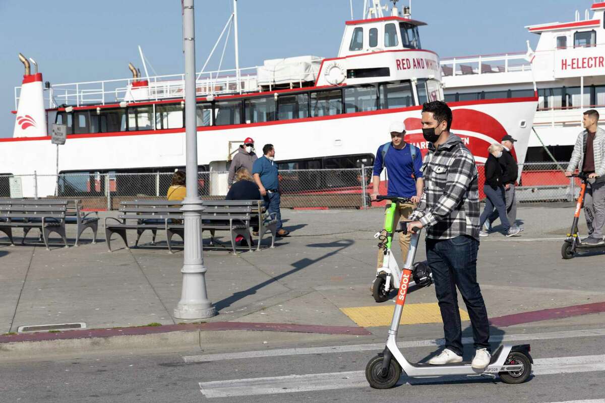 People ride scooters at Fisherman’s Wharf in February. International tourism has lagged in S.F.