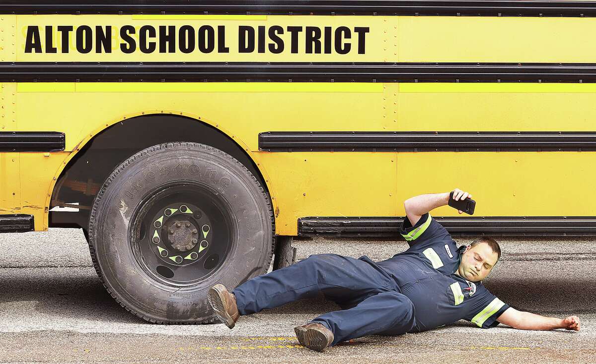 John Badman|The Telegraph A representative from the Alton School District's bus garage rolls out from under the school bus after photographing the damage to the rear wheels and axle of the bus. The bus was involved in a crash Monday that injured two people.