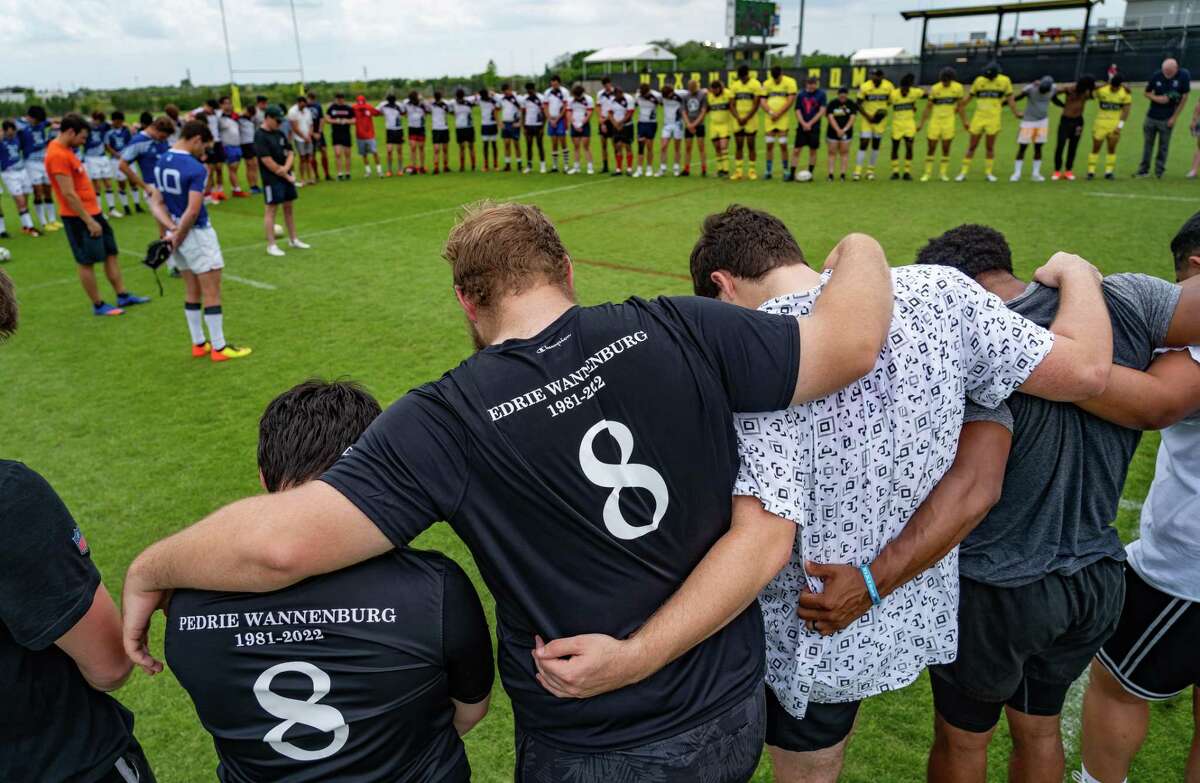 Rugby players lock arms during a moment of silence before a memorial rugby tournament held to honor the memory of Pedrie Wannenburg, a South African rugby player and coach who had a profound influence on the game in Houston including coaching at Rice University, on the practice fields at Aveva Stadium on Saturday afternoon, April 30, 2022, in Houston. Wannenburg was killed in a car crash earlier in April.