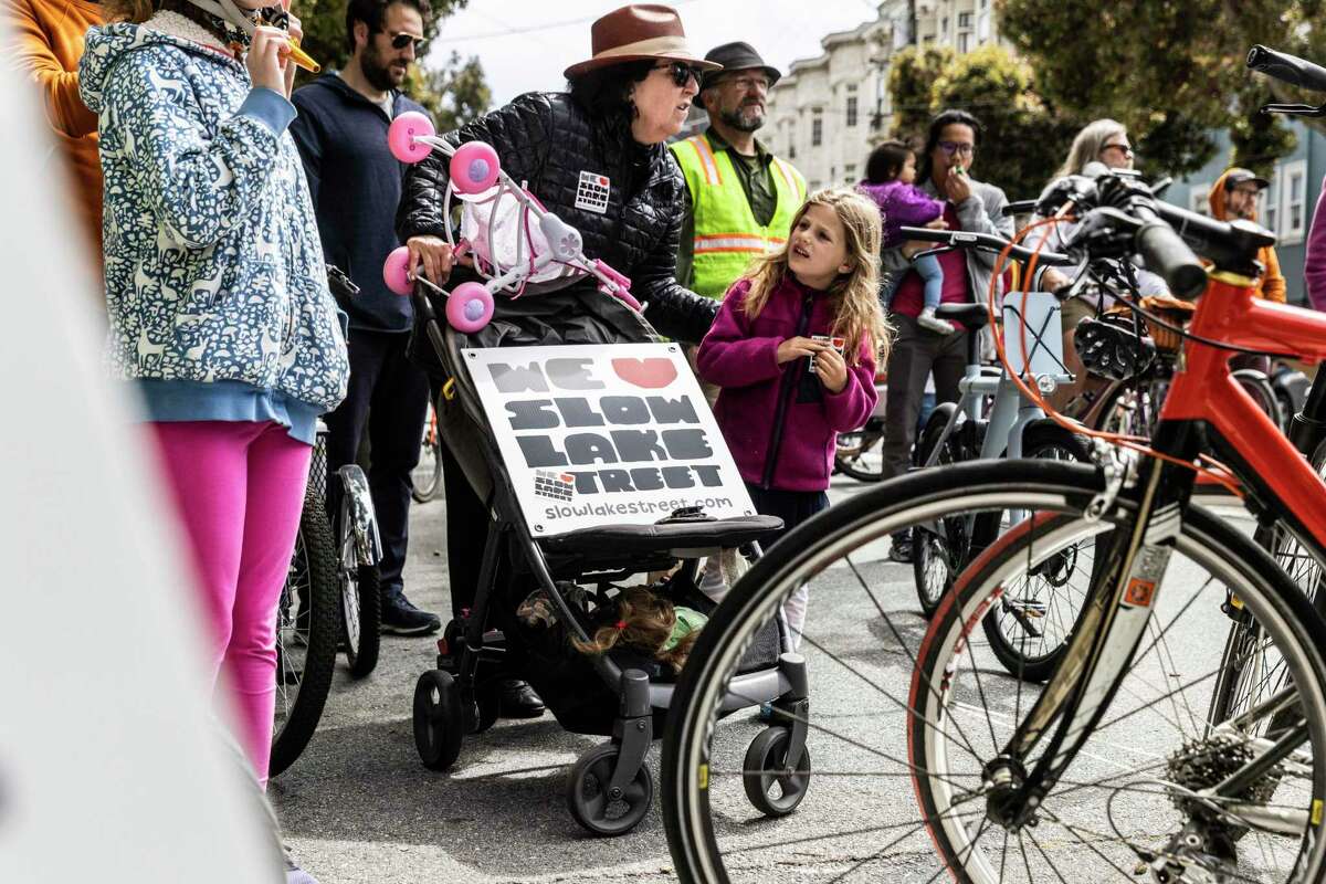 Lake Street resident Anita Friedman, center, listens to a speaker as she participates in a community parade with her grandchildren in San Francisco in support of keeping permanent many of the Slow Street designations created during the pandemic lockdown.